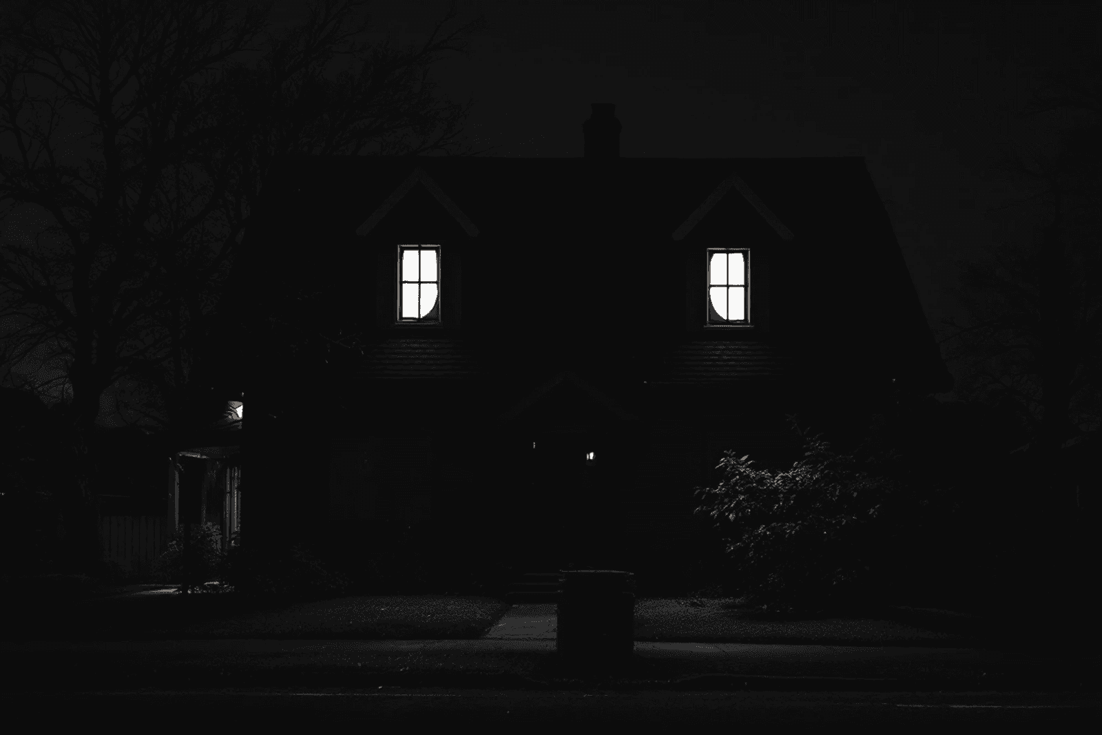 A dark house with two crescent-shaped attic windows, seen at night.