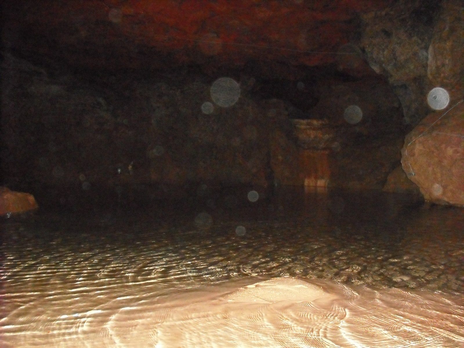 A dark cave with a still pool in the foreground, lit bright from the camera, and pale grey circles of different sizes hanging in the air above the water.