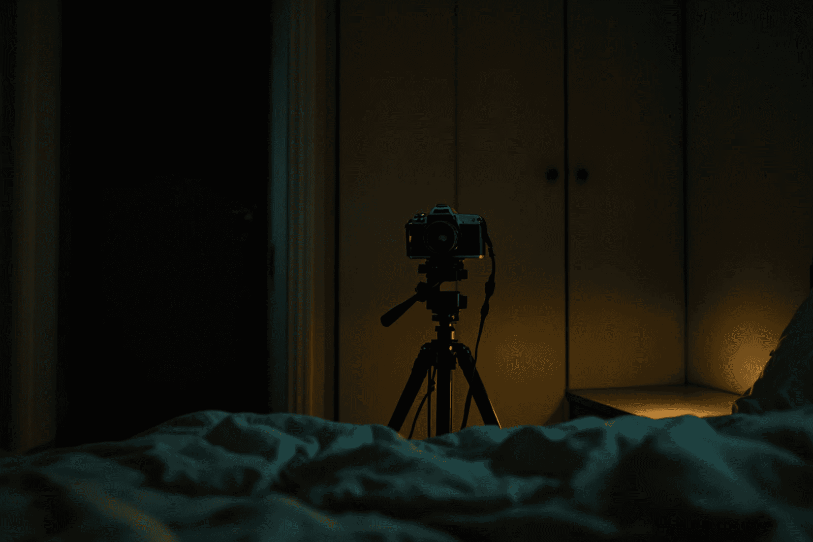 A tripod camera at the foot of a bed, its indicator light glowing.